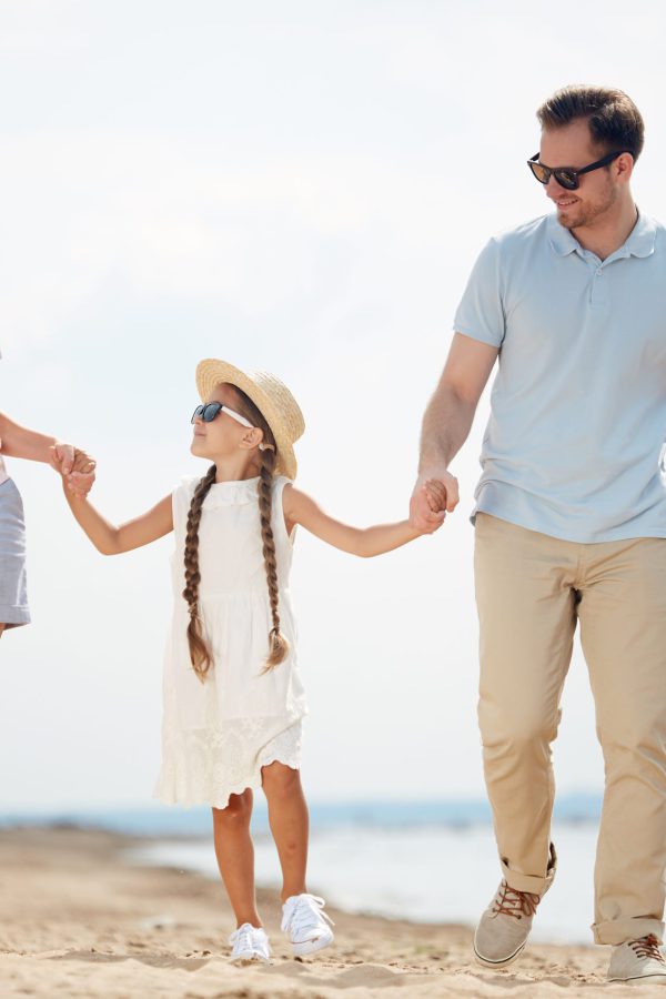 Full length portrait of modern happy family holding hands while enjoying walk on beach during Summer vacation